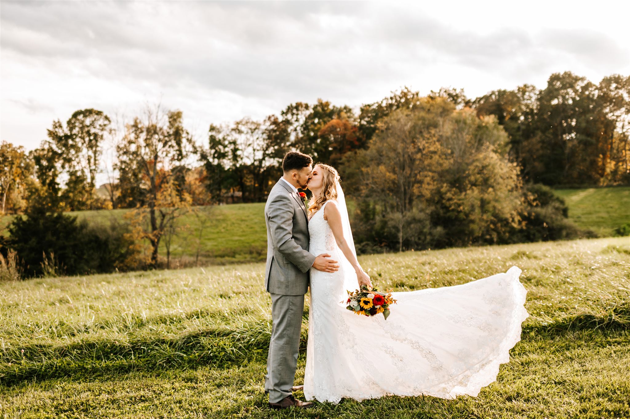 bride and groom kissing as the brides wedding dress blows in the wind in a field at their outdoor Charlottesville wedding venue