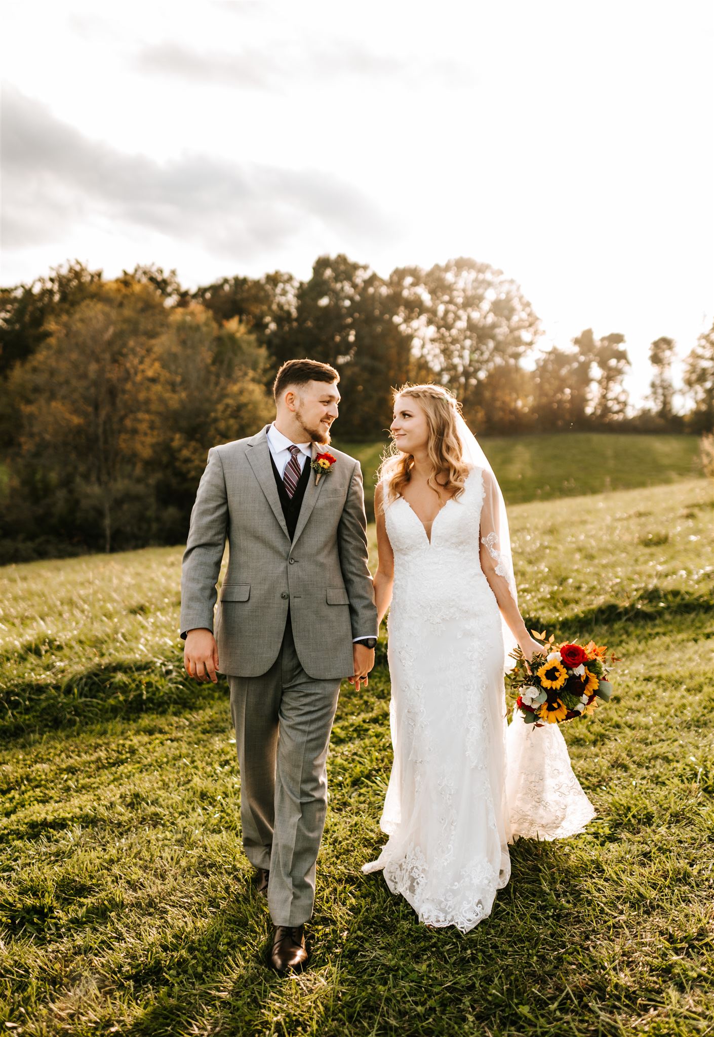 bride and groom holding hands and walking through a field together while the sun sets in the distance for their Shenandoah National Park Wedding with Charlottesville wedding photographer