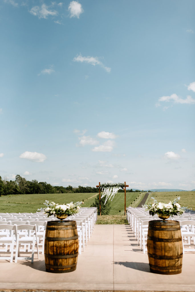 outdoor ceremony space at Shenandoah Valley wedding venues with white chairs, barrels and other wedding decor with simple white florals captured by Virginia wedding photographer 