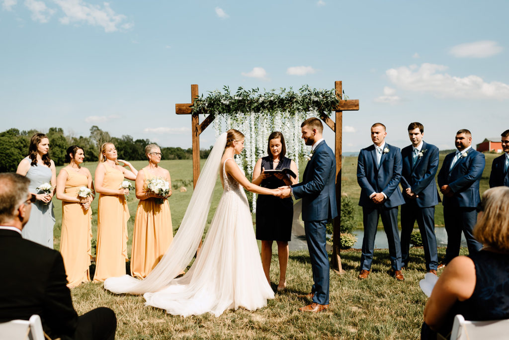 bride and groom holding hands during their wedding ceremony as their officiant marries them at their outdoor Shenandoah wedding venue with Charlottesville wedding photographer 