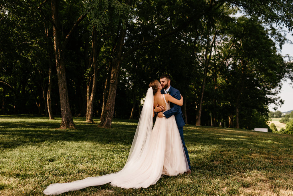 bride and groom embracing each other and kissing in a grove of trees for their outdoor Charlottesville wedding 