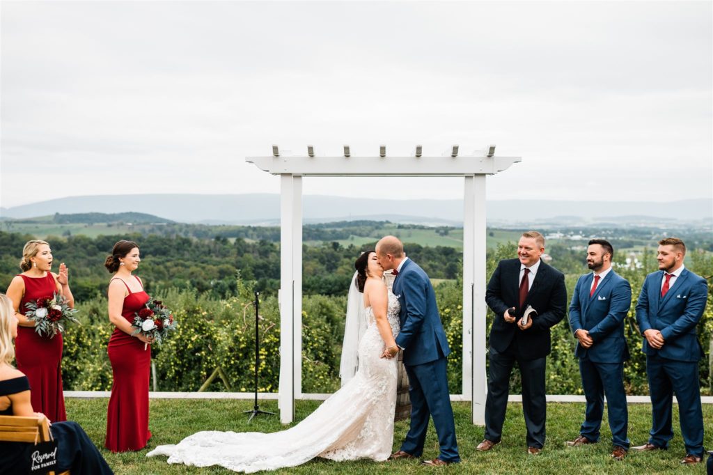 outdorr wedding ceremony with bride and groom kissing under an arch while holding hands at Shenandoah wedding venue with Charlottesville wedding photographer 