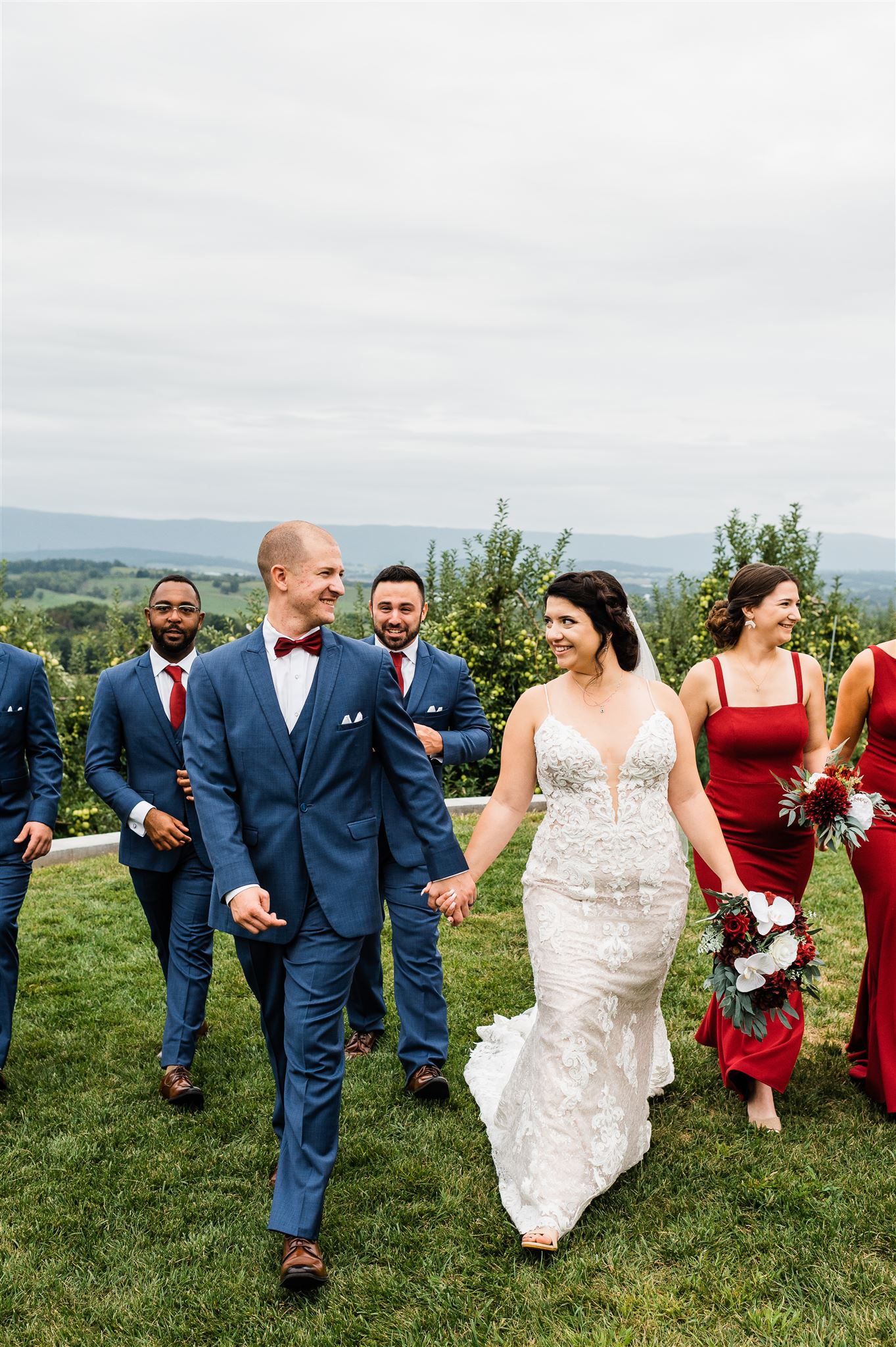 bride and groom holding hands and walking with their bridal party captured by Charlottesville wedding photographer at Charlottesville wedding venue in the hills