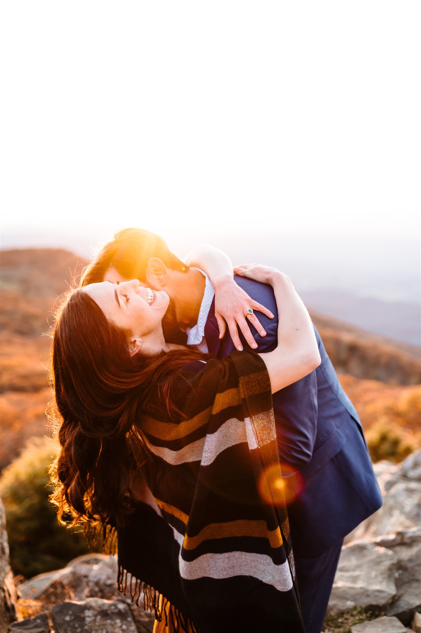 man and woman hugging on top of a mountain and laughing as the sun sets for their engagement photos with Charlottesville wedding photographer