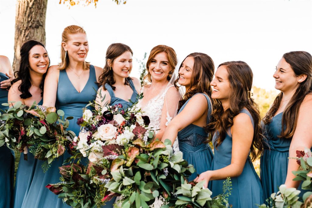 bride standing with her bridesmaids who are in blue bridesmaids dresses holding their wedding bouquets together as they laugh for the Shenandoah National Park wedding with Charlottesville wedding photographer 