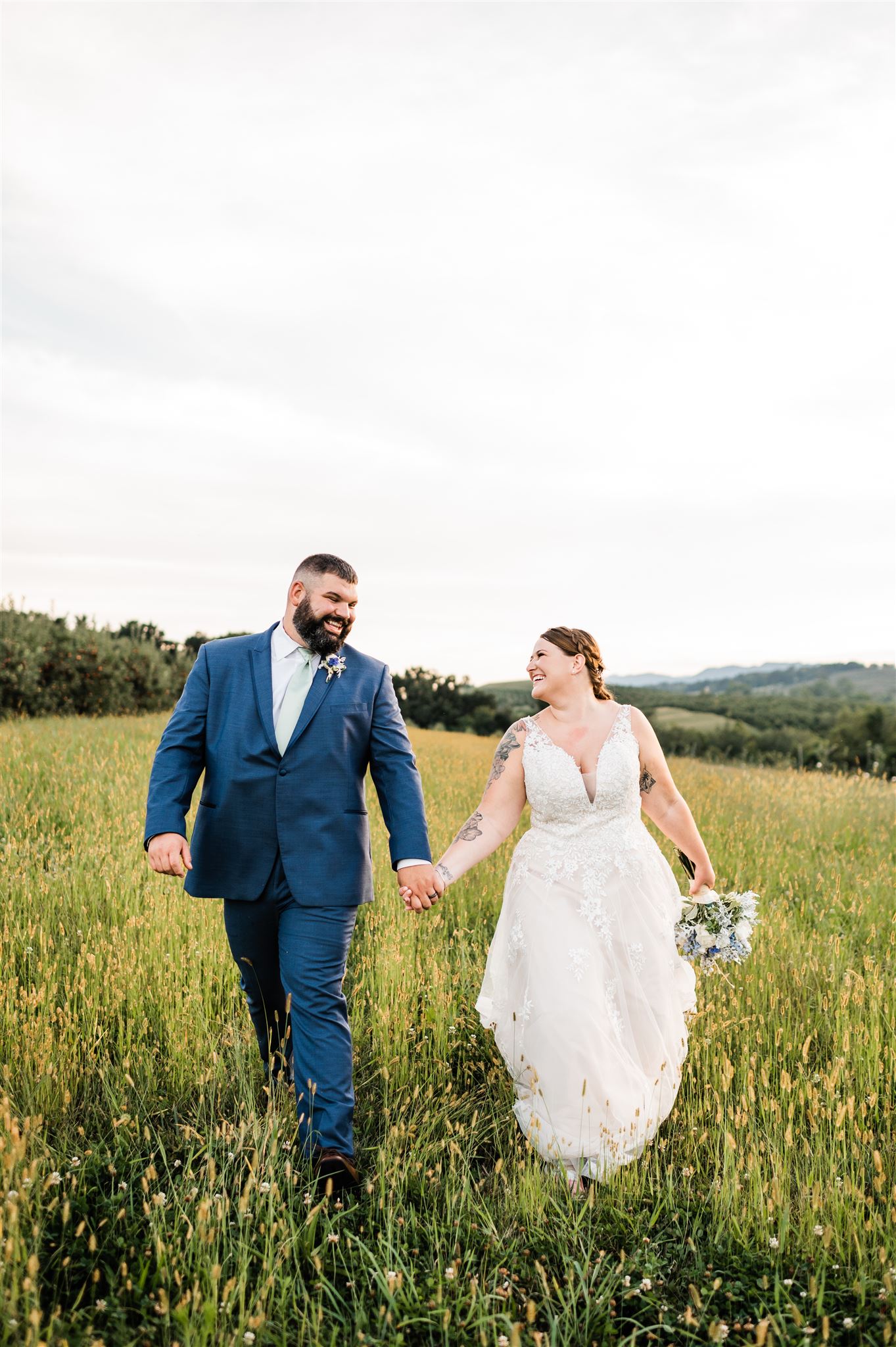 bride and groom hold hands and wlak through a golden field together as they look at each other and smile taken by Charlottesville wedding photographer