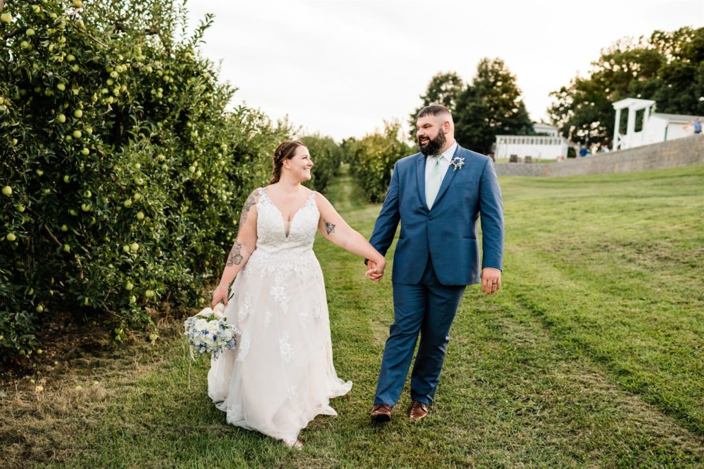bride and groom holding hands and walking through an orchard for their Shenandoah wedding with Charlottesville wedding photographer 