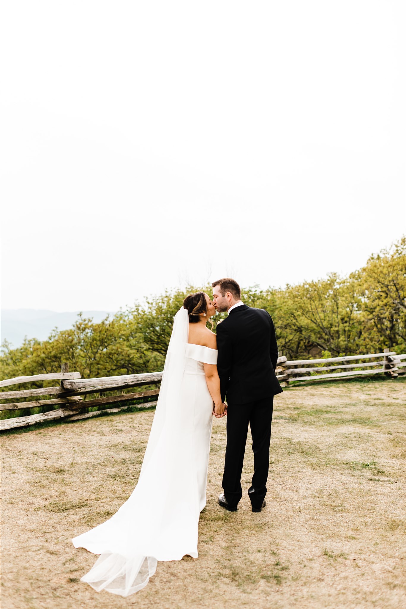 Shenandoah National Park Wedding with bride and groom holding hands and walking on a mountain top while leaning in to kiss each other
