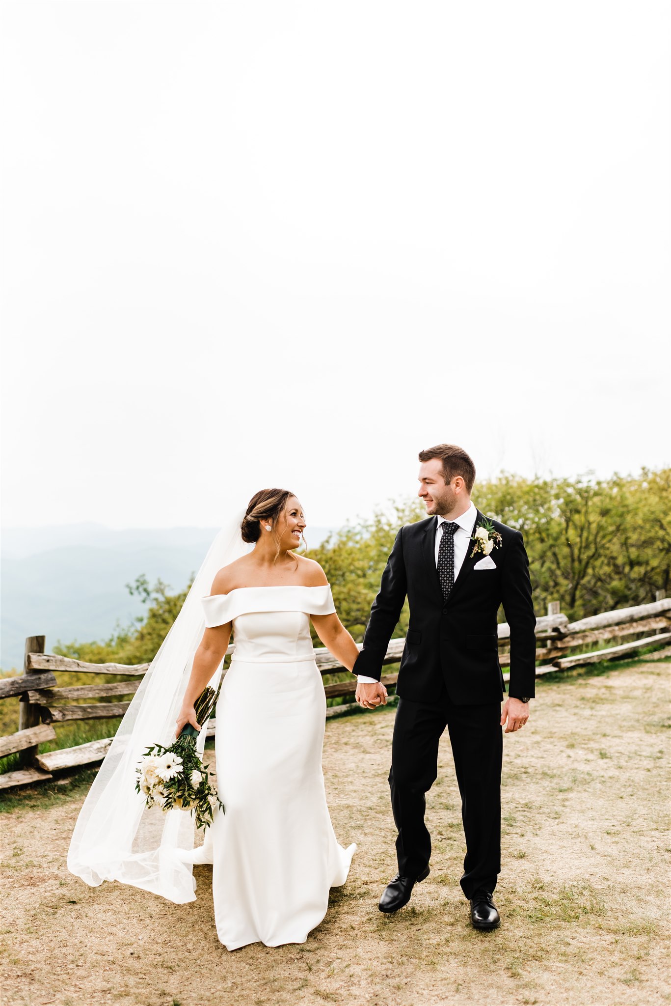 Shenandoah National Park Wedding with bride and groom holding hands and smiling at each other as they walk on a trail in the mountains for their outdoor wedding