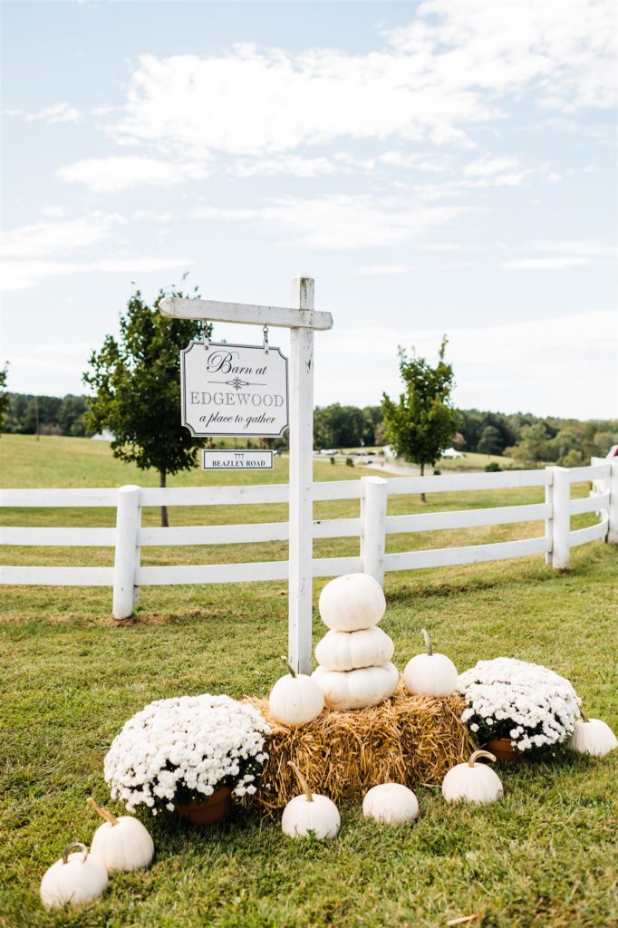 Charlottesville wedding photographer photographs wedding signage at a barn wedding venue with white flowers and pumpkins surrounding it