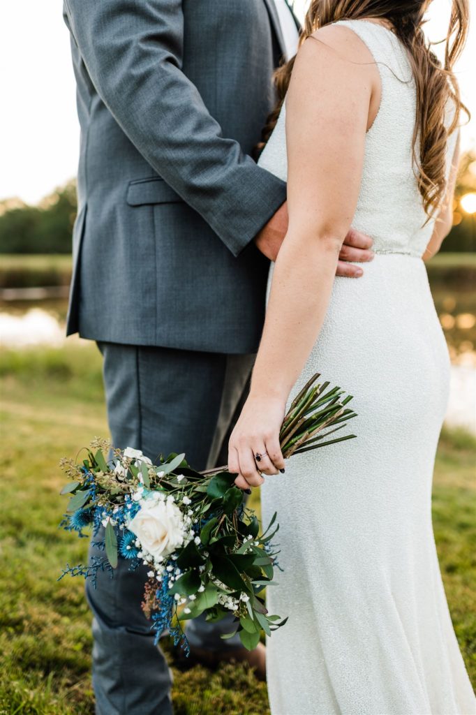 detail shot of bride holding her blue floral wedding bouquet as her groom holds her waist for their Shenandoah wedding