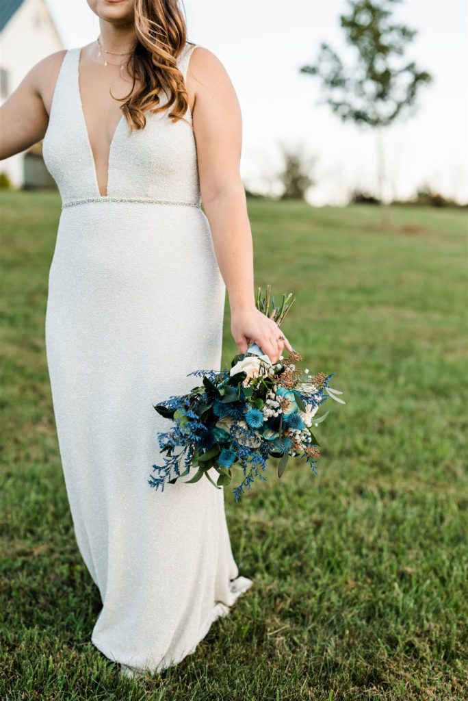 bride holding her blue wedding bouquet to her side as she walks through a wedding venue in Shenandoah wedding venue captured by Charlottesville wedding photographer