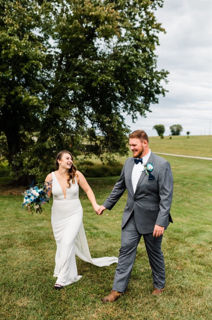bride and groom holding hands and walking through a field together at their outdoor Shenandoah wedding venue captured by Charlottesville wedding photographer
