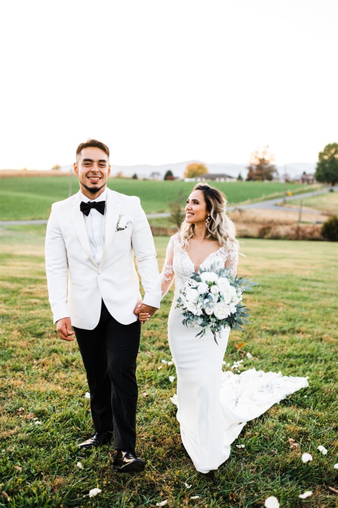 Charlottesville wedding photographers captures Shenandoah wedding with bride and groom holding hands and walking through a field together with hills in the distance
