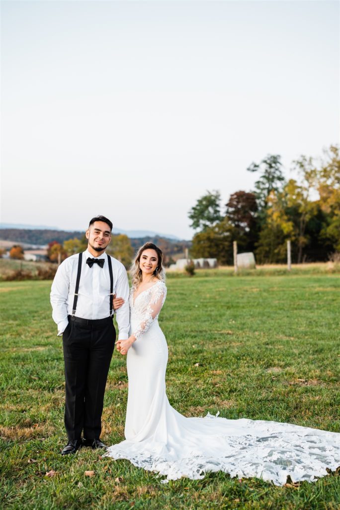 bride and groom posing in a field together while holding hands in a field at an outdoor Shenandoah wedding valley captured by Charlottesville wedding photographer