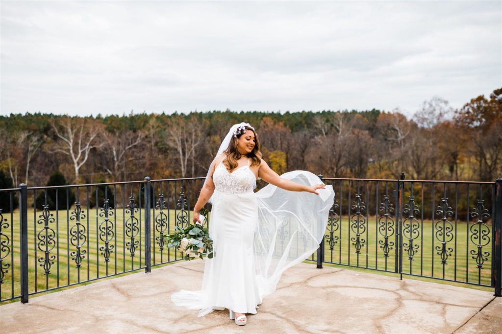 outdoor bridal photos with bride on a porch of her wedding venue as they waves her veil in the air captured by Charlottesville wedding photographer 