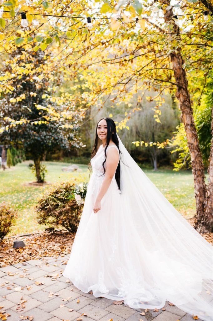 bride in a tulle and floral lace wedding dress walking in a courtyard of a Shenandoah wedding venue looking over her shoulder with fall trees surrounding her photographed by Charlottesville wedding photographers