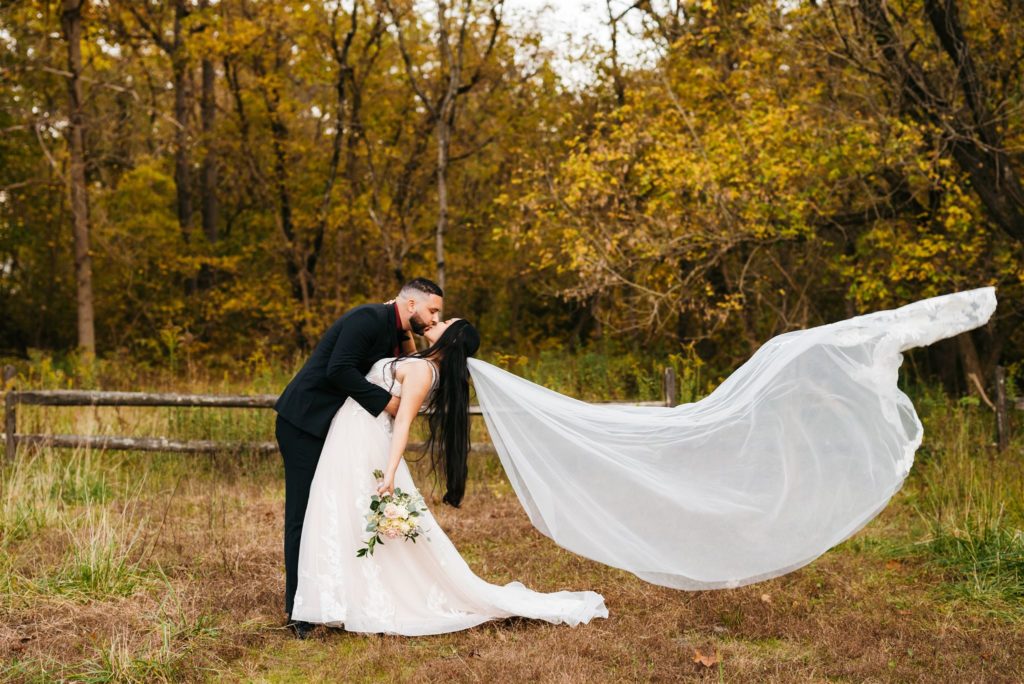 outdoor wedding photos with groom dipping his bride backwards and kissing her as her veil flows in the wind behind her captured by Charlottesville wedding photographers 