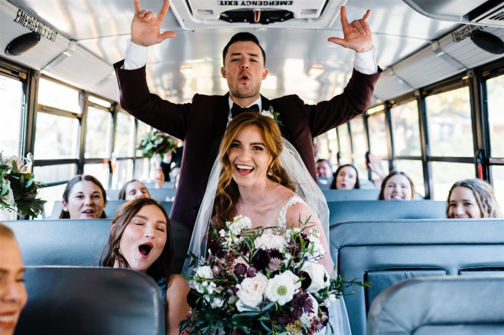 bridal party in a bus together as the bride and groom stand in the aisle and pose while laughing captured by Charlottesville wedding photographer 