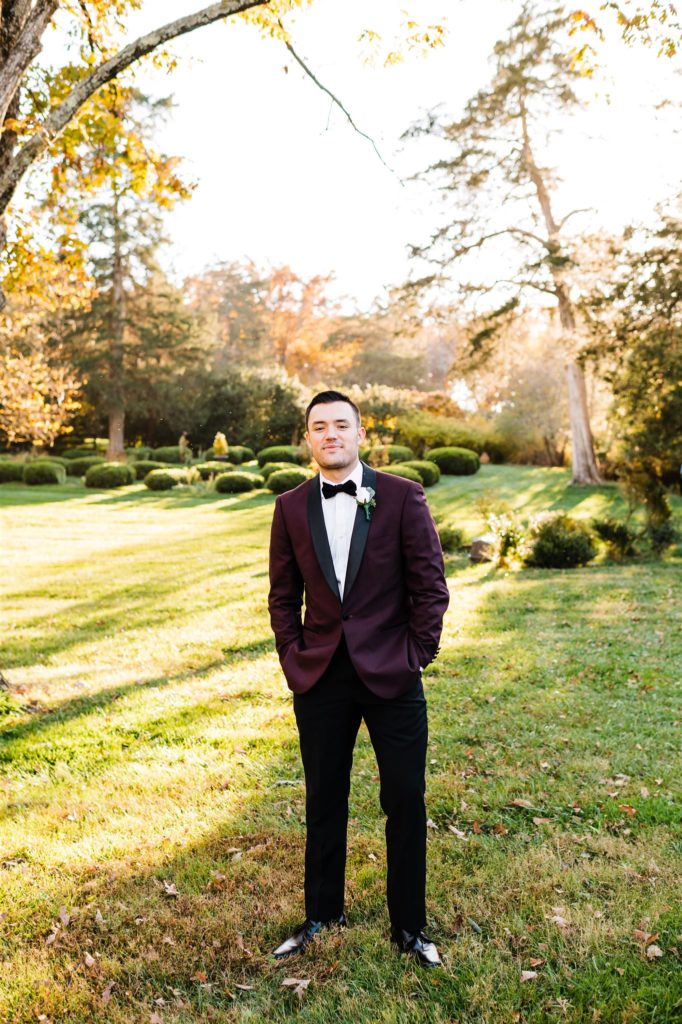 Shenandoah wedding with groom posing in a dark red suit coat in a field at his outdoor wedding venue by Charlottesville wedding photographer 