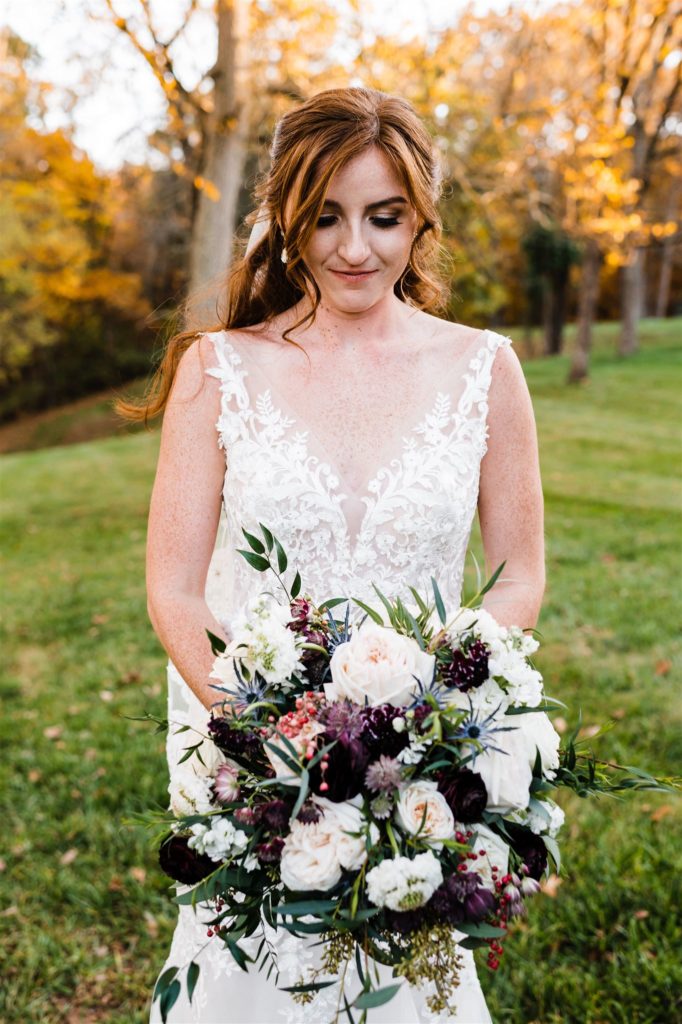 Charlottesville wedding photographer photographs bride in a lace wedding dress holding a white rose bouquet with a purple floral detail at Shenandoah wedding