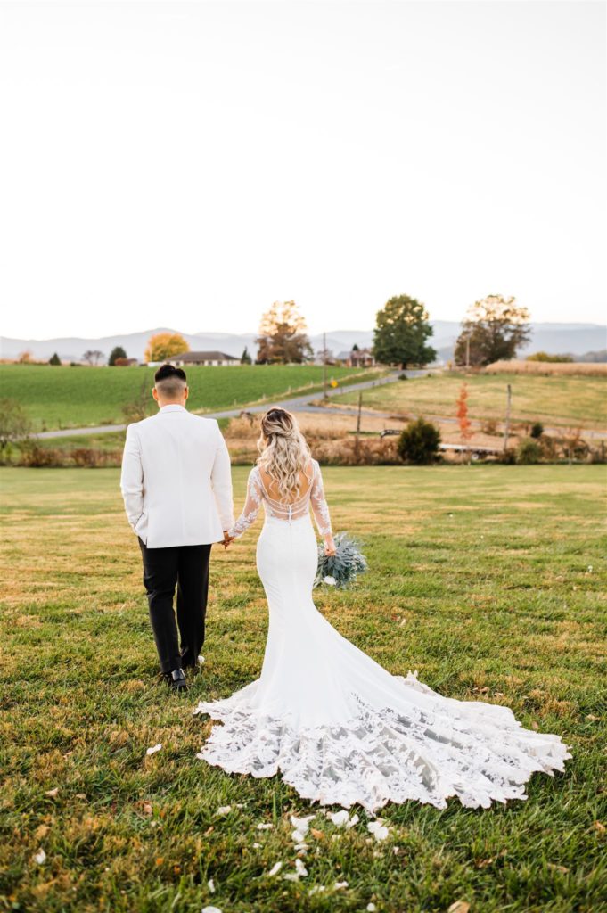 Virginia wedding photographer captures outdoor bridal portraits with bride nad groom holding hands and walking down a hill together at their Shenandoah Valley wedding venues 
