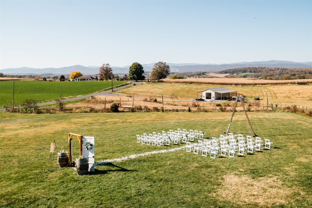 Virginia wedding photographer photographs outdoor wedding ceremony space with white chairs and barn themed details in an open field in Shenandoah Valley wedding venues 