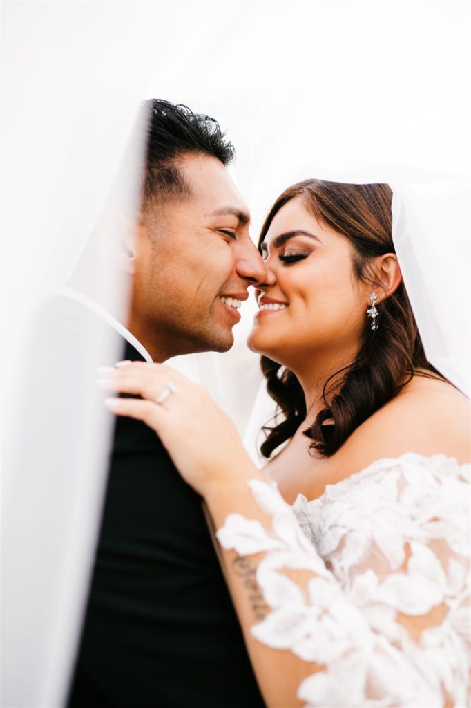 bridal portraits with Charlottesville wedding photographer capturing bride and groom under the brides veil and they lean into each other smiling while the bride embracing her grooms shoulder