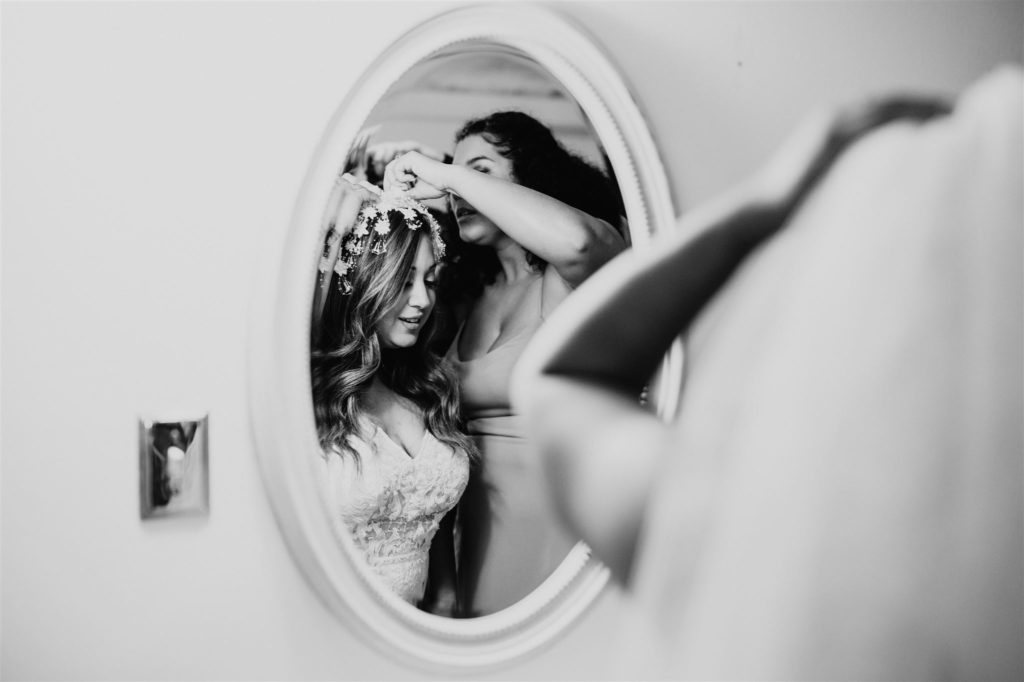 bridesmaid helping the bride put on her wedding veil in a mirror captured by Charlottesville wedding photographer 