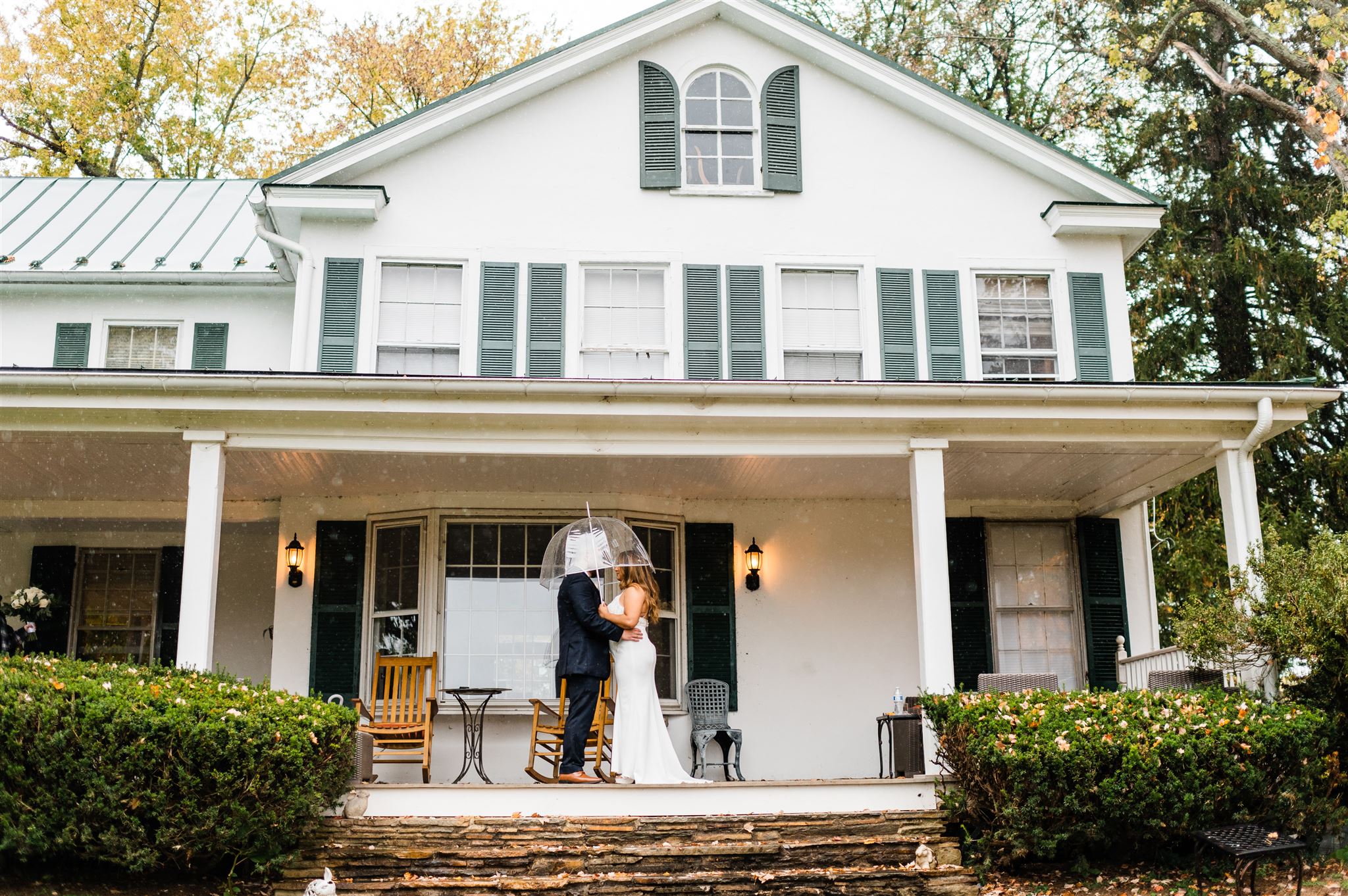 rainy day wedding pictures with bride and groom under a clear umbrella as they stand on the porch of their Shenandoah wedding venue together