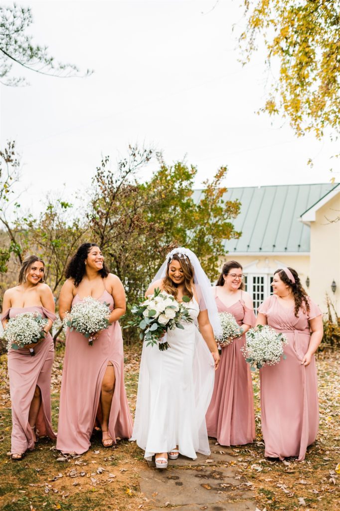 bride walking with her bridesmaids who are wearing pink bridesmaids dresses on the lawn of a Shenandoah wedding venue captured by Charlottesville wedding photographer 