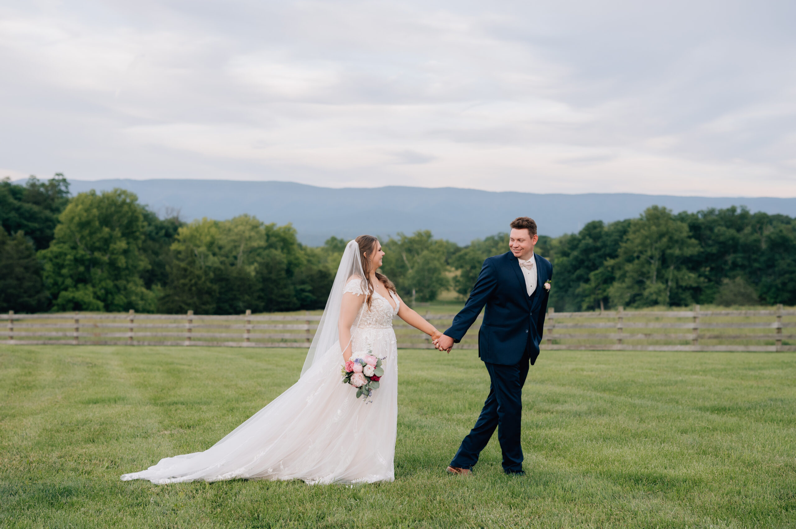 Virginia Wedding Couple walking in a field embracing one another with the mountains in the distance captured by Virginia wedding photographer