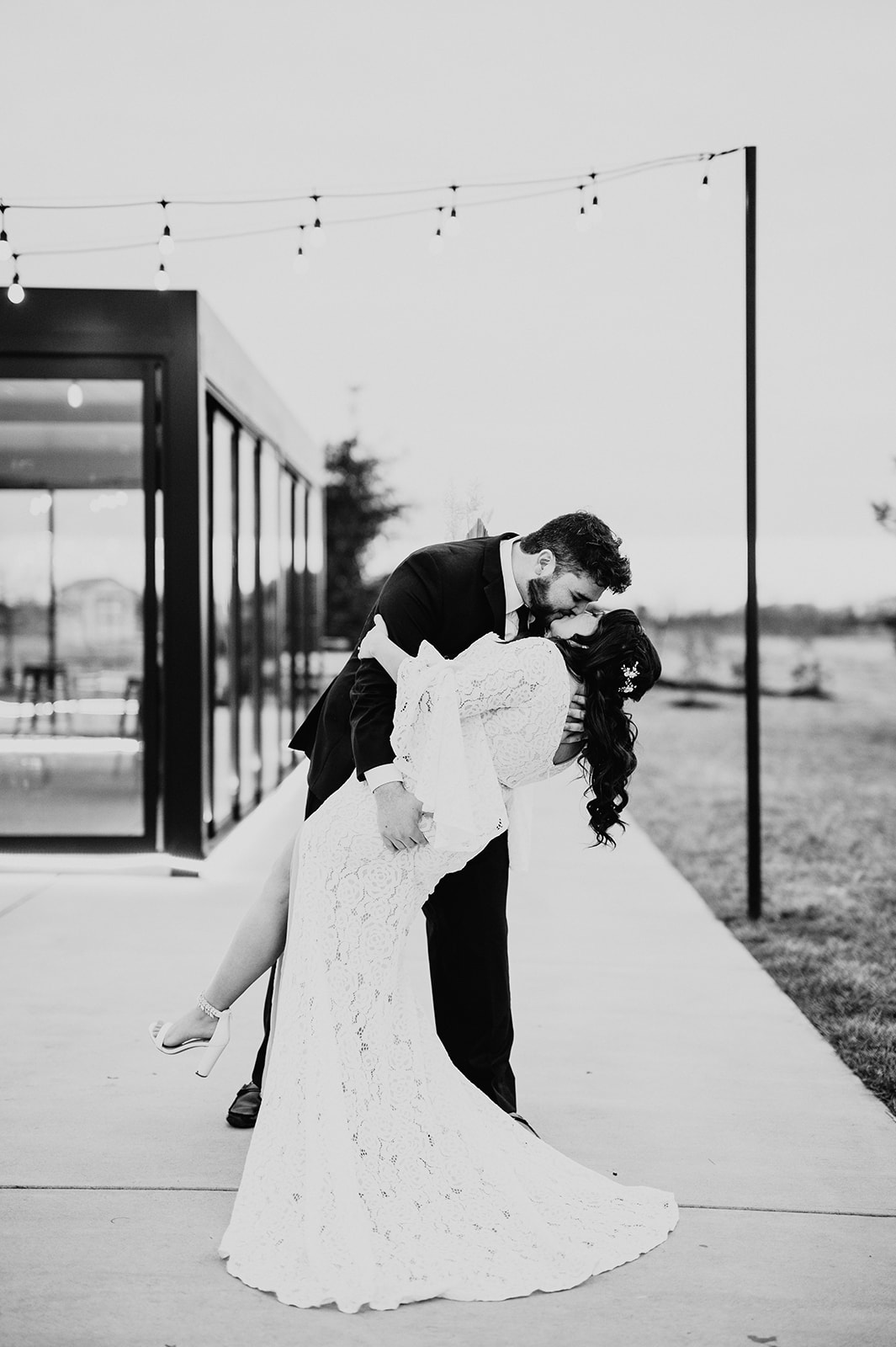 black and white wedding photo with groom dipping his bride backwards and kissing her passionately as he holds her waist