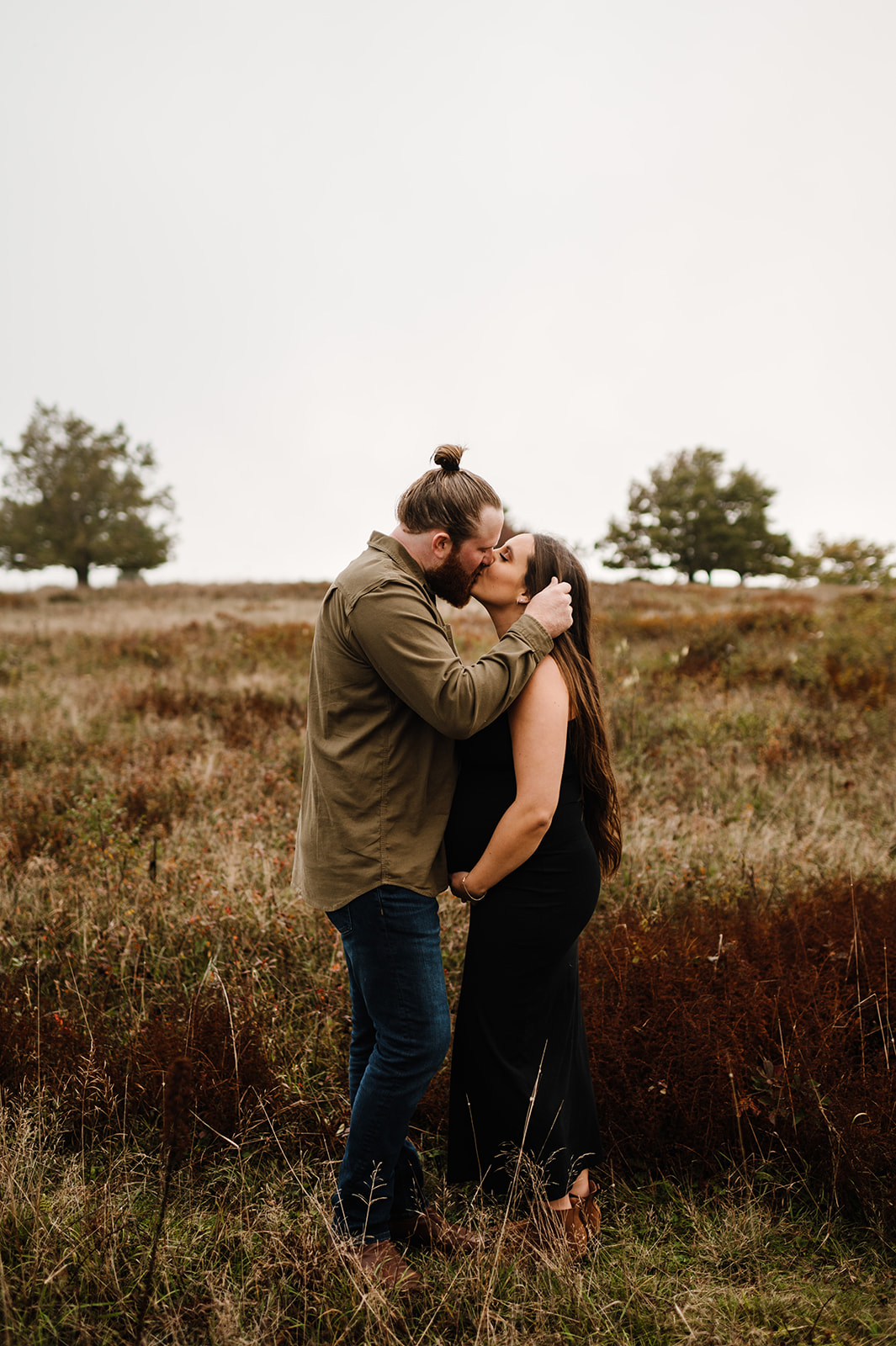 A romantic moment captured between an expectant couple sharing a kiss in an open meadow. The serene natural setting highlights the intimate connection, making it a perfect example of maternity photos in Shenandoah National Park.