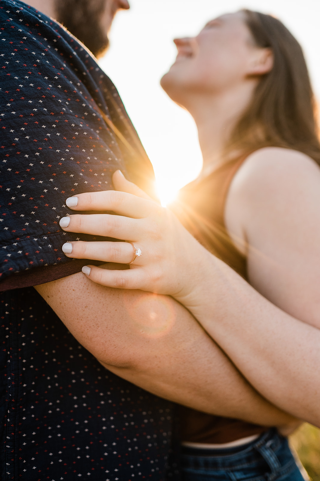 A close-up of an engagement ring on a woman's hand as she holds her partner's arm, with warm sunlight and a soft, romantic focus during their Charlottesville engagement session.