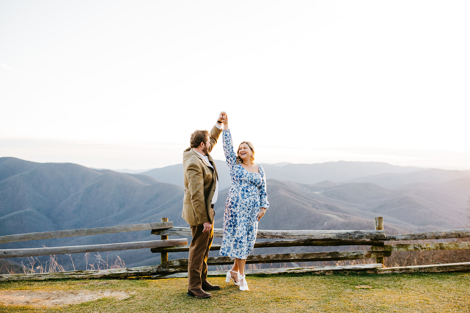 charlottesville wedding photographer captures engagement photos at blue ridge overlook with couples dancing on the overlook with a wood fence behind them with the mountains in the distance