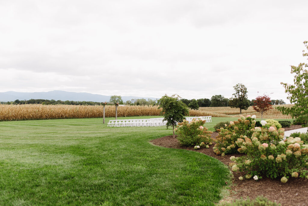 Charlottesville wedding photographer photographs An outdoor wedding ceremony setup at Frieden Farms in Shenandoah, featuring a wooden arbor adorned with floral accents and rows of white chairs on a lush green lawn