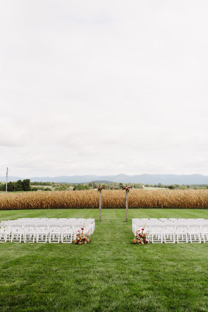 Shenandoah wedding venue with a view of the mountains and full fields in the distance with white wooden chairs set up on the lawn of the ceremony space