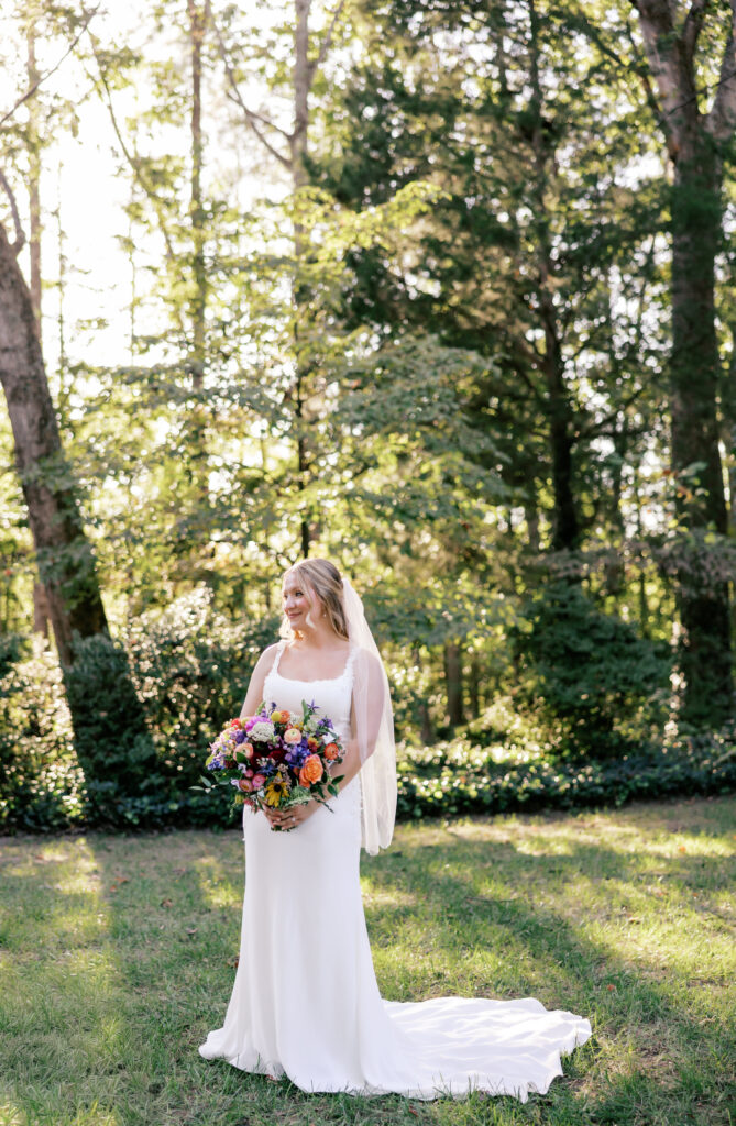 bride in white dress with fall bouquet surrounded by green foliage at golden hour at Seven Springs, VA