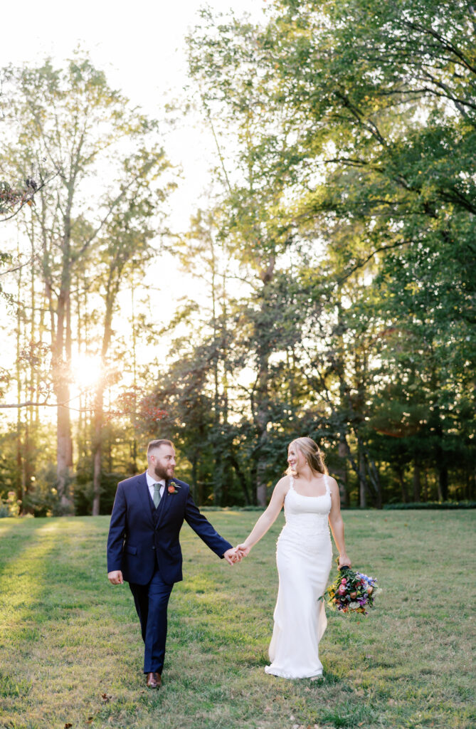 groom and bride walking at golden hour with sunlight beaming through the trees at Seven Springs, VA