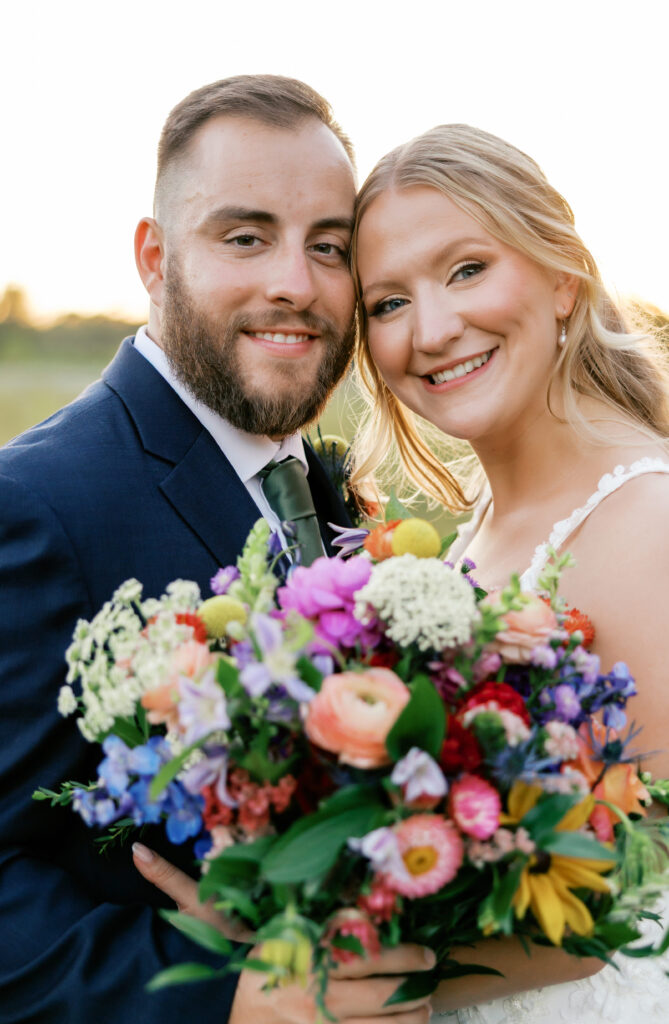 Zoey and Brandon smiling at the camera with the fall bouquet surrounded by warm sunset at golden hour