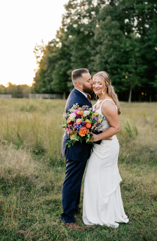 Zoey and Brandon embracing with the fall bouquet surrounded by warm sunset at golden hour in a field of grass at Seven Springs, VA