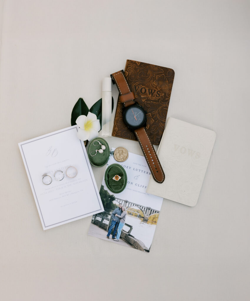 Wedding flat lay details of invitation, wedding rings, groomsmen watch and vows booklet