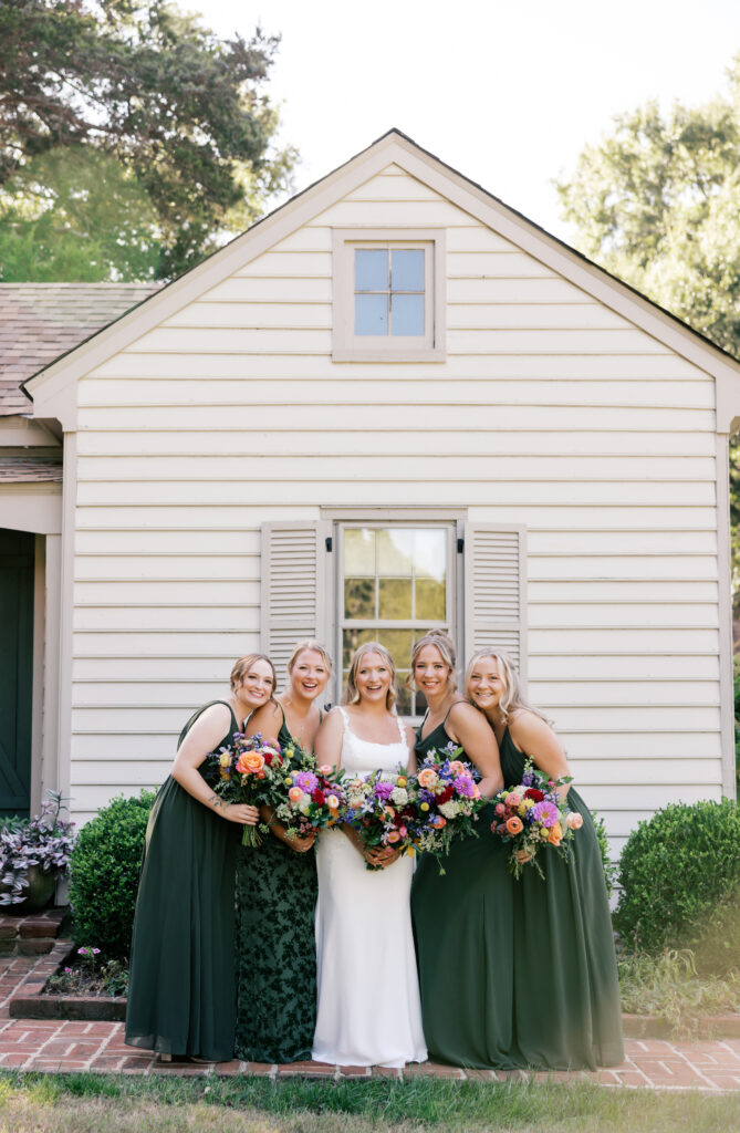 Bride Zoey smiling with her bridesmaids in matching green dresses in front of the guest house of Seven Springs.